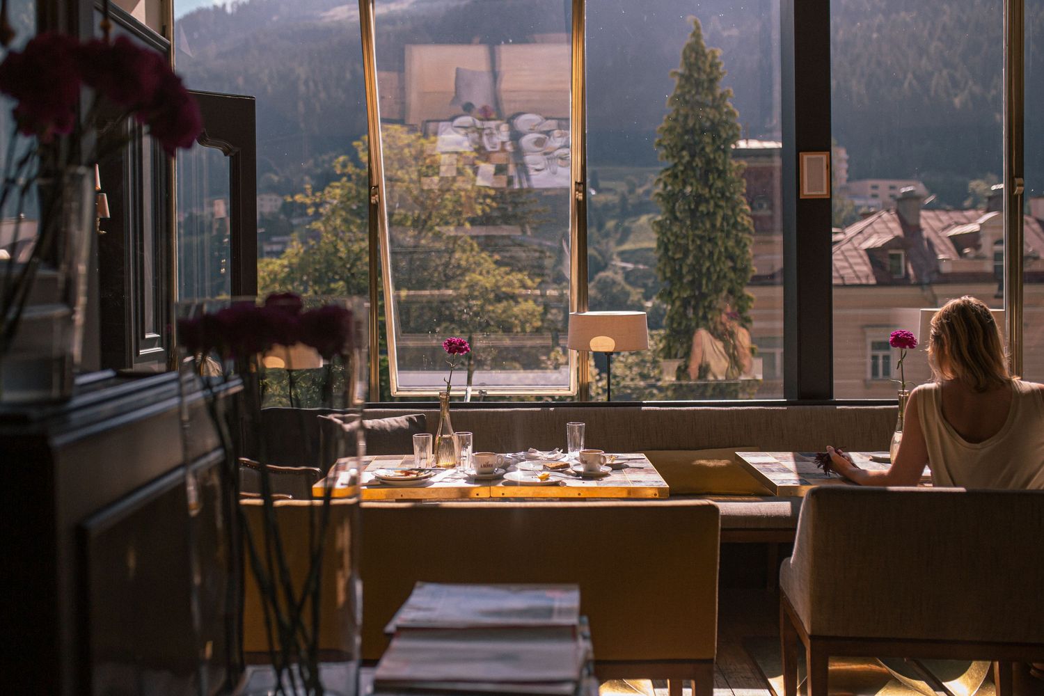Person sits at a cafe table near large windows overlooking a mountain town on a misty morning. Hotel photography with feeling.