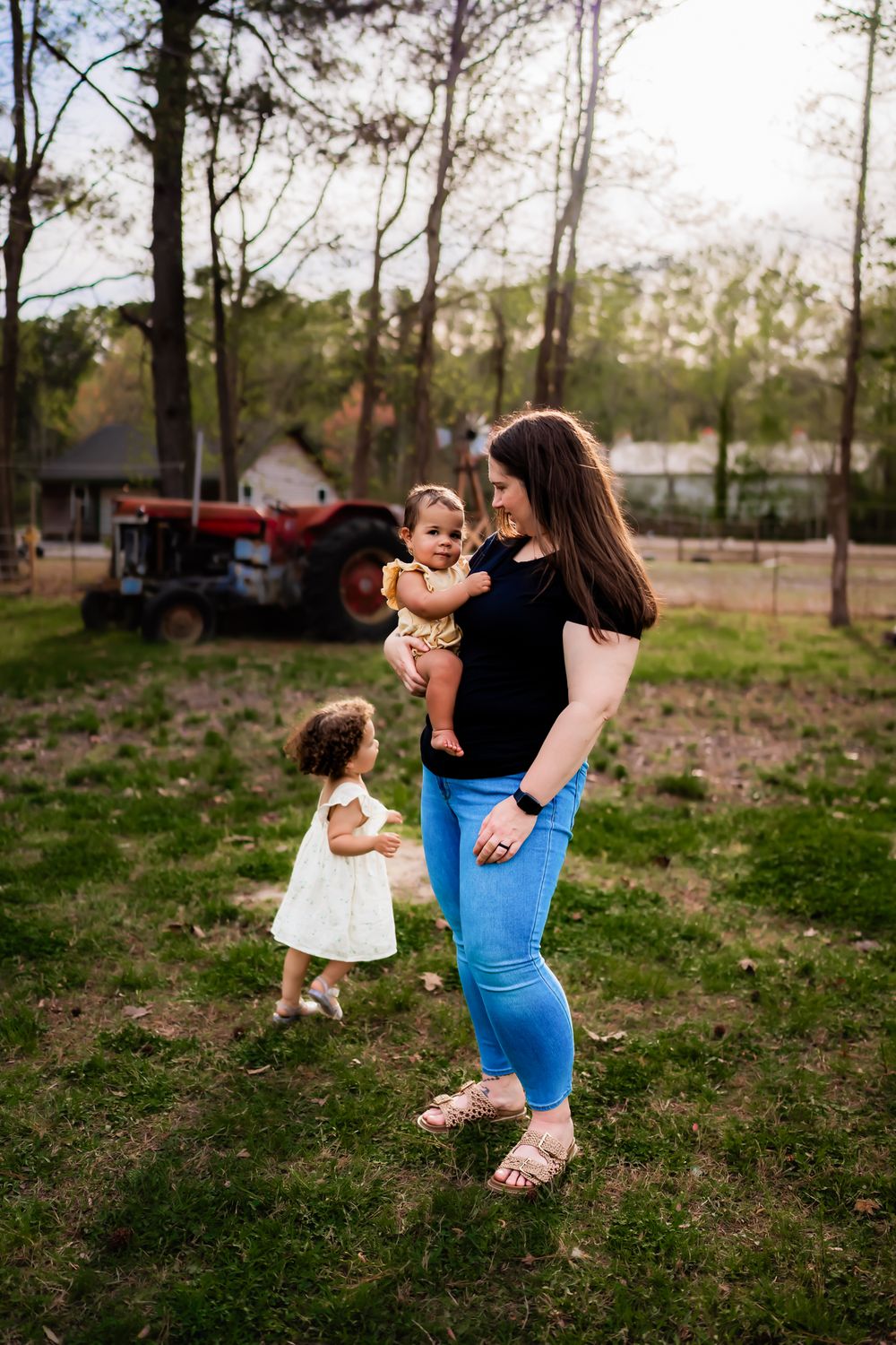 A tender outdoor family moment captured in a rustic setting with trees and a red tractor in the background.