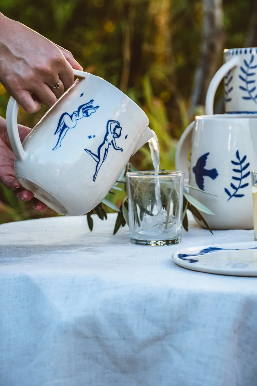 Service de thé en extérieur, main versant du thé blanc dans une tasse en porcelaine décorée.