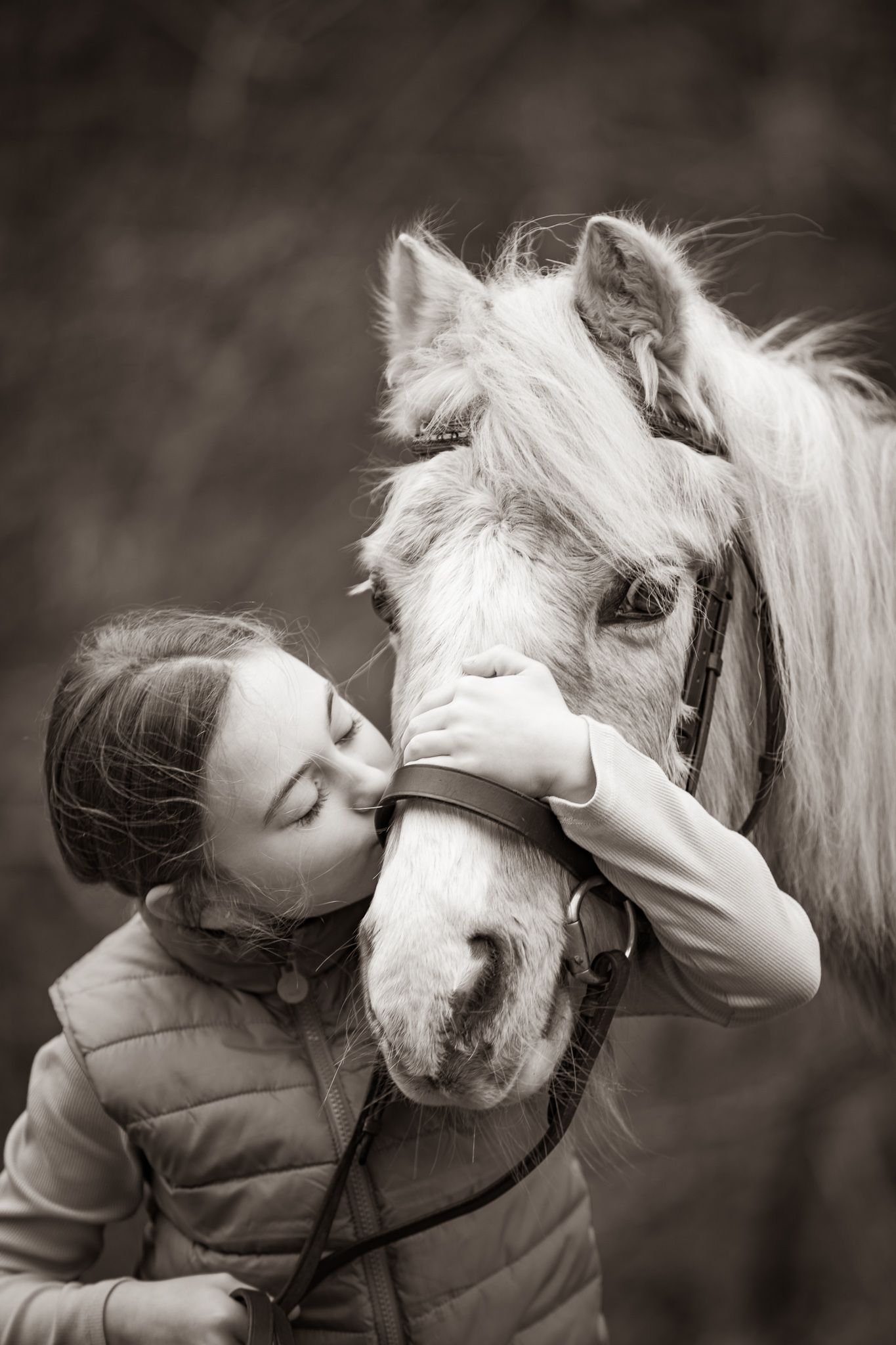 A serene black and white portrait of someone in a flowy dress standing with a majestic white horse in a pastoral setting.