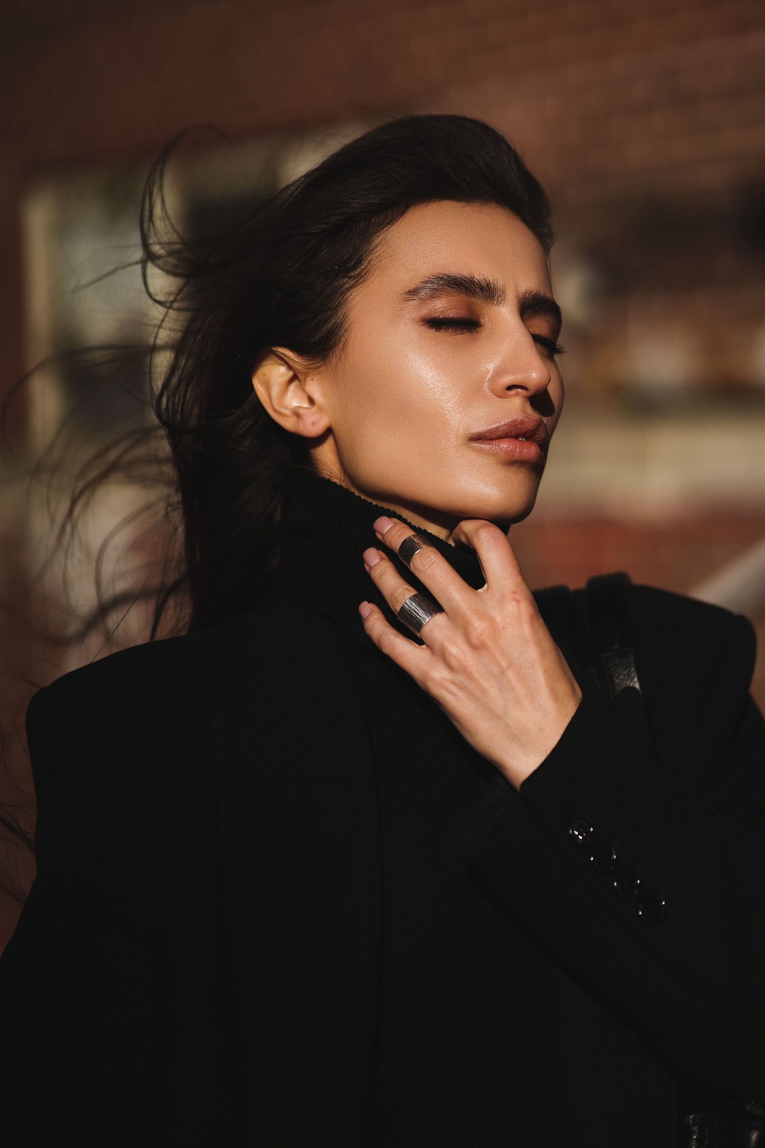 Dramatic portrait in warm lighting showing person in black turtleneck with windswept hair.