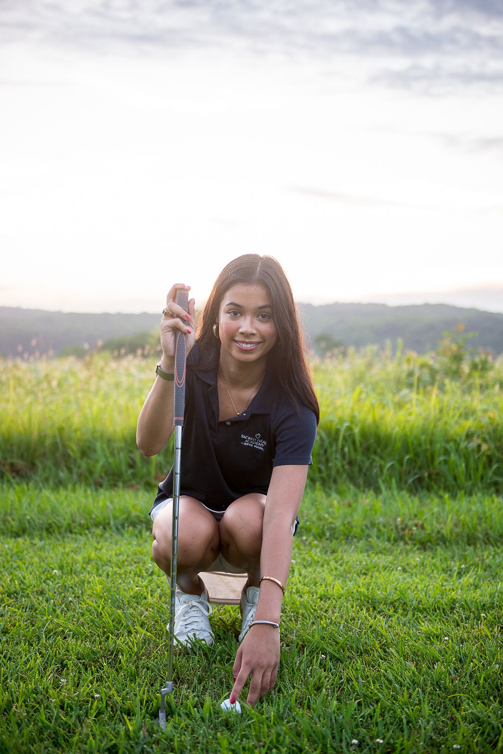 Woman in black t-shirt lies on grass in front of mountain landscape during golden hour.