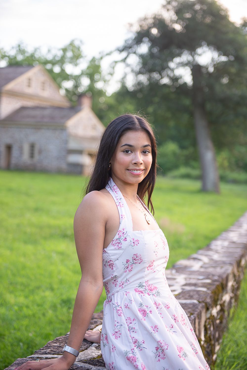 A summer photo session in a field with a white floral dress against a stone wall and green background.