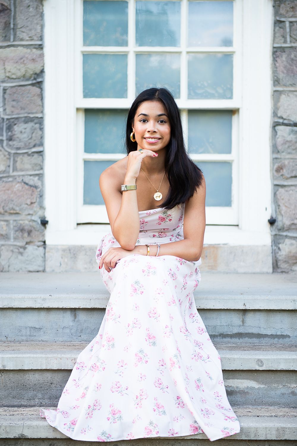A person in a floral pink dress poses on stone steps against a building with windows.