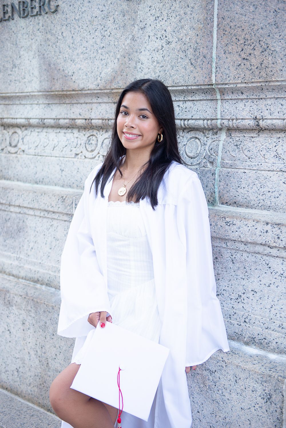 White graduation gown against textured stone wall with classic architectural details.