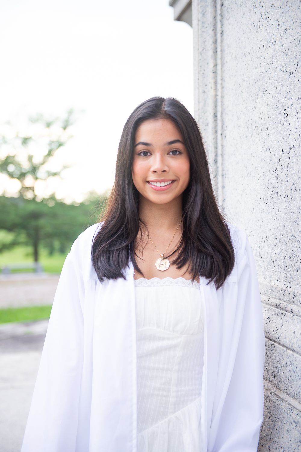 A person in a white outfit smiles warmly against a bright stone architectural backdrop.
