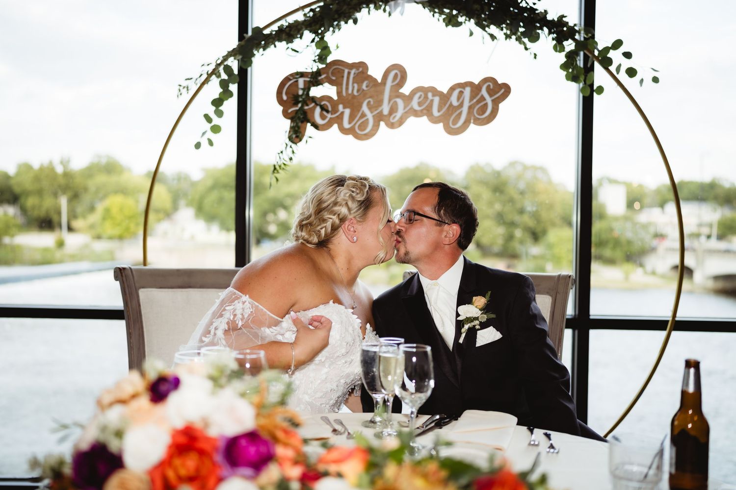 Wedding party members share a toast during a reception with colorful floral centerpieces and wine glasses on the table.