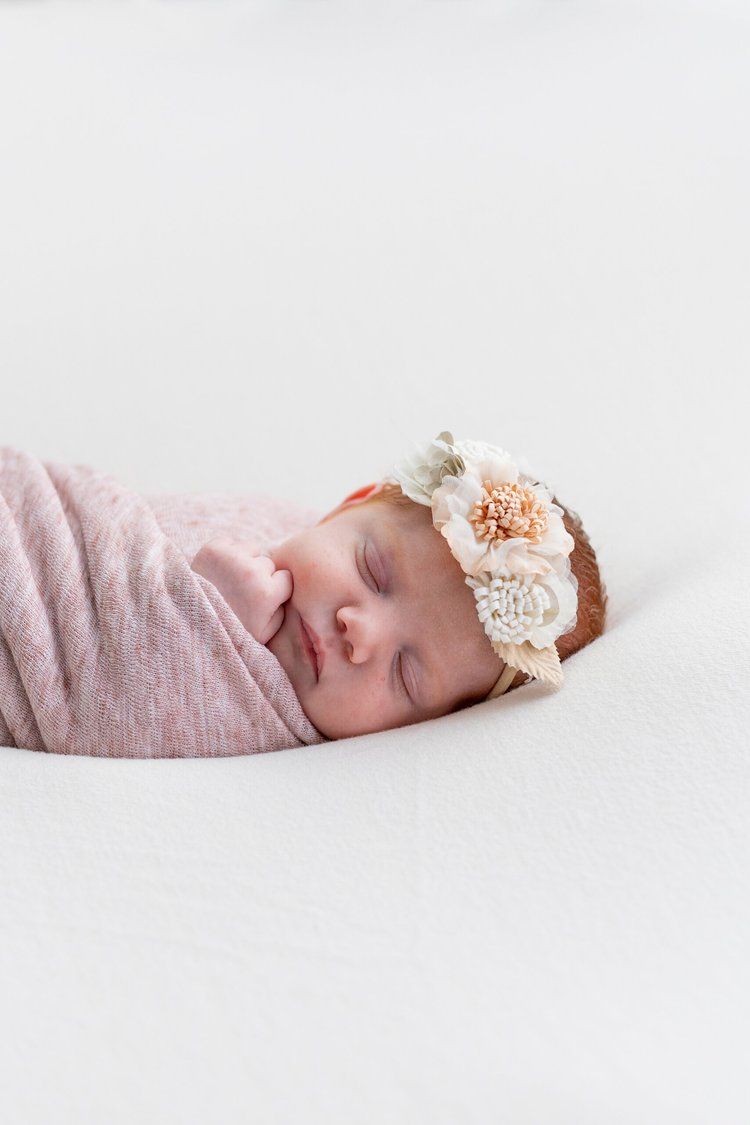 Sleeping newborn wrapped in pink swaddle with floral headband.
