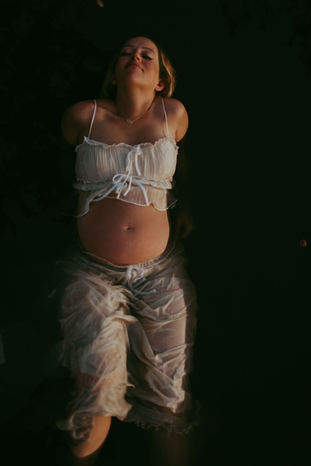 A person wearing white lingerie and bloomers poses against a dark background in a series of artistic photographs. sarasota photographer