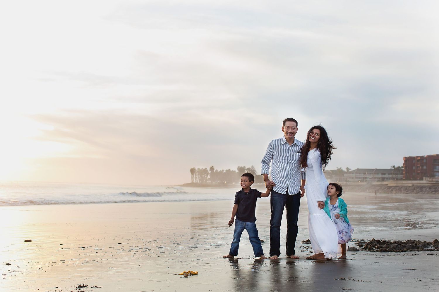 A family stands together by the ocean shore during sunset on a tranquil beach as waves roll in softly at their feet.