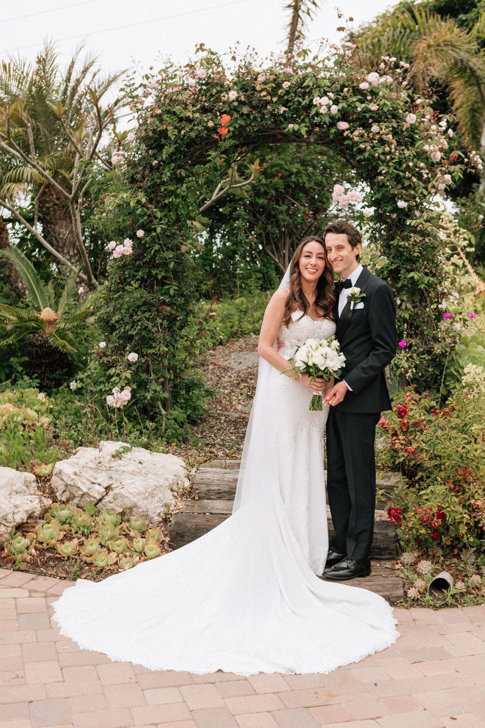 Malibu elopement photographer capturing a smiling couple under a lush floral arch.