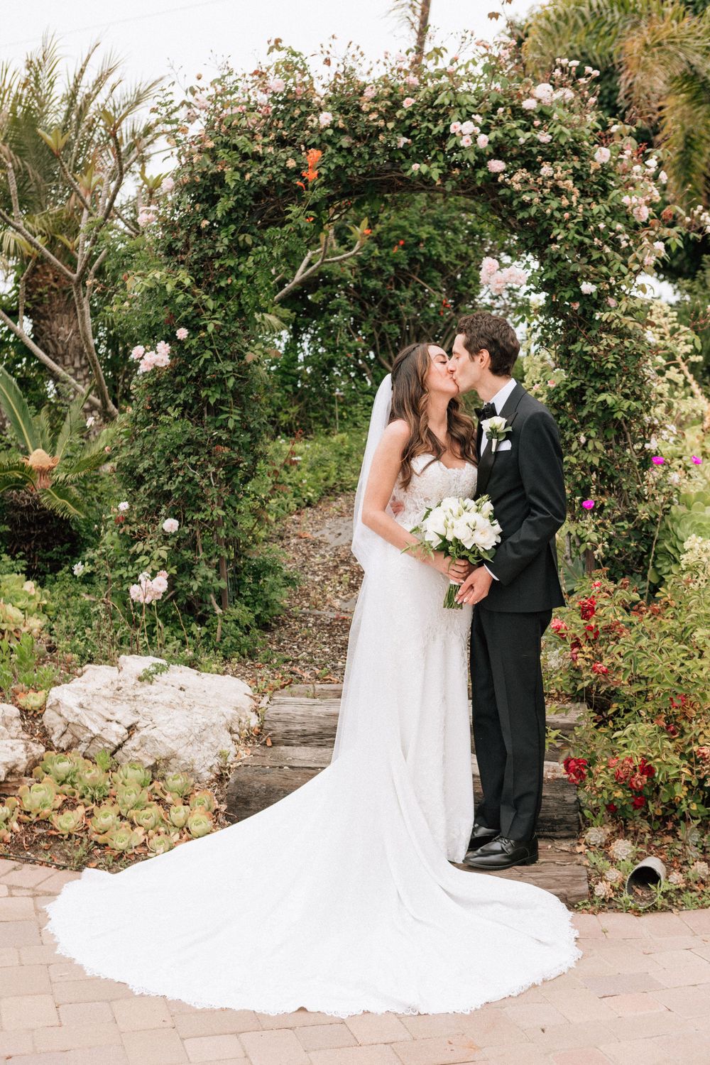 Malibu elopement photographer capturing a kiss under a lush floral arch.