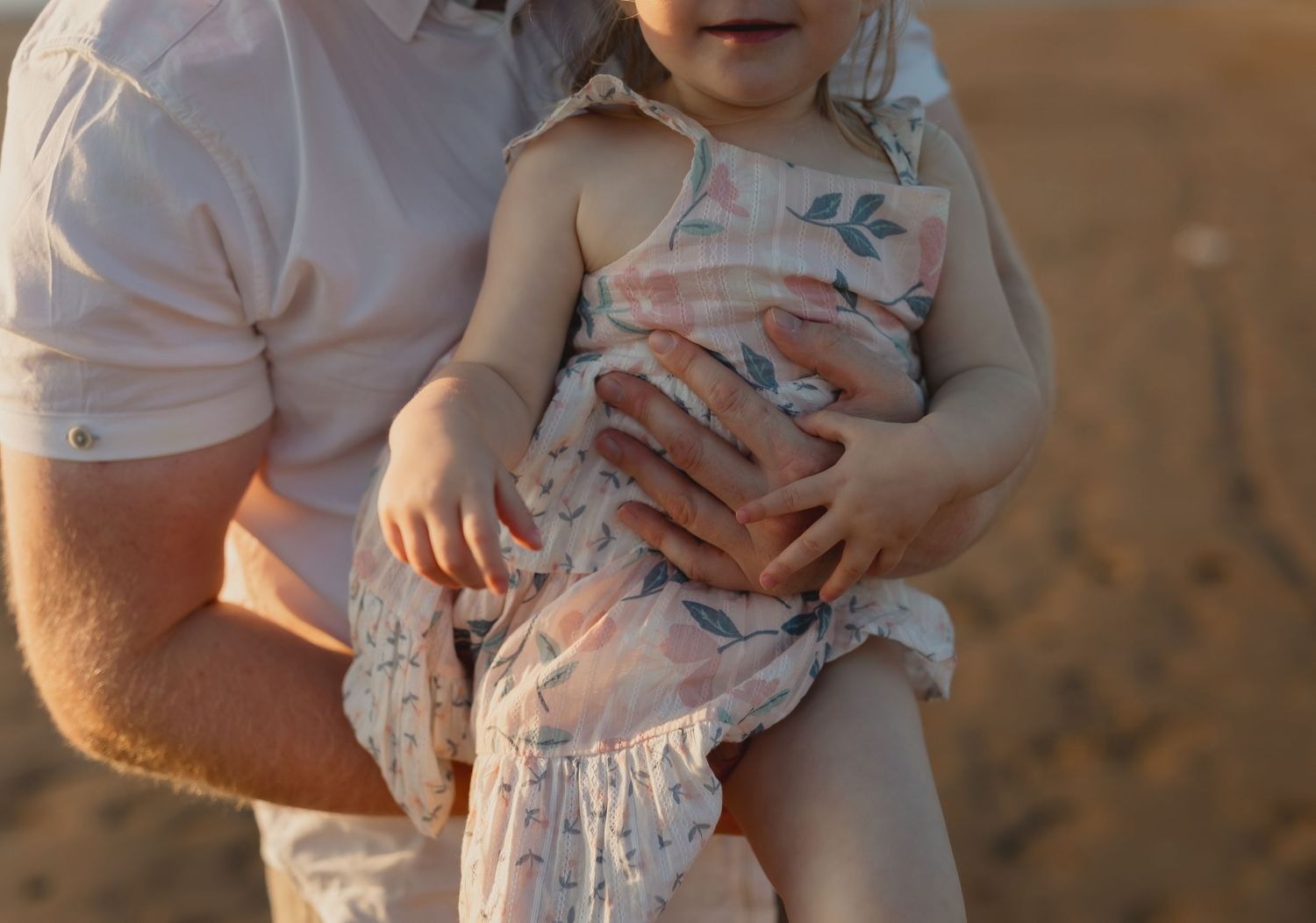Parent holding child's hand during golden sunset in outdoor setting.