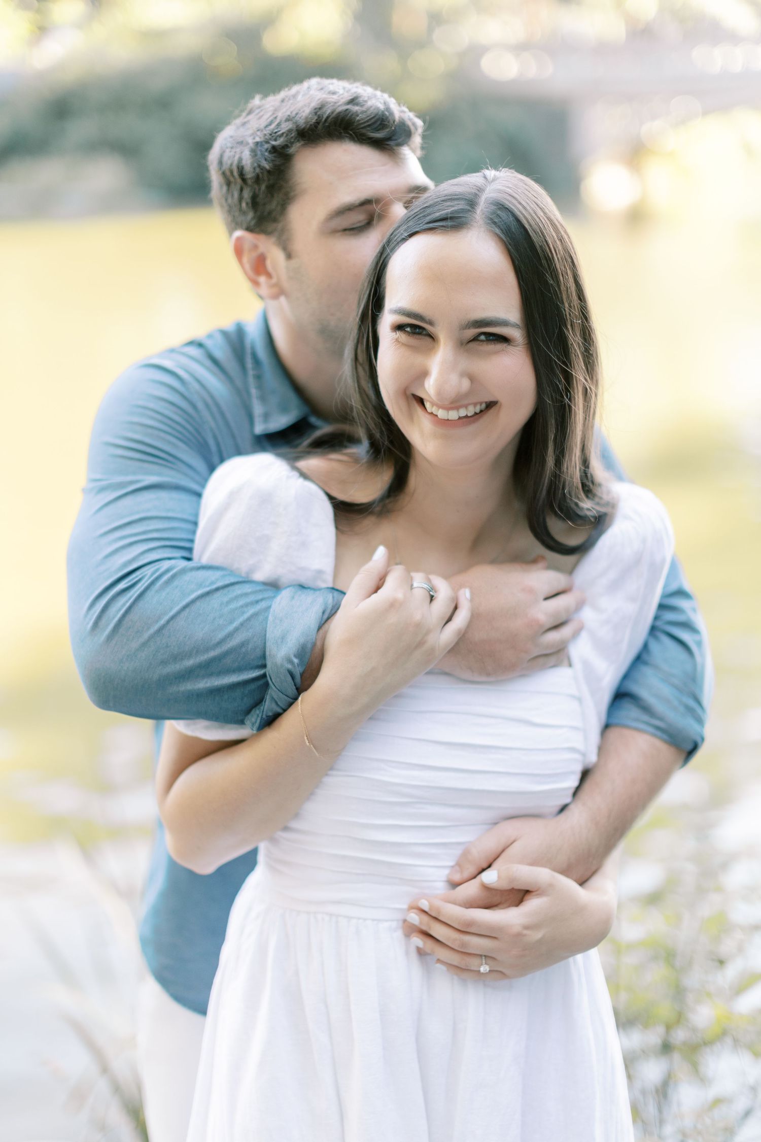 Intimate outdoor photo series featuring couple in blue shirt and white dress embracing in golden sunlight.