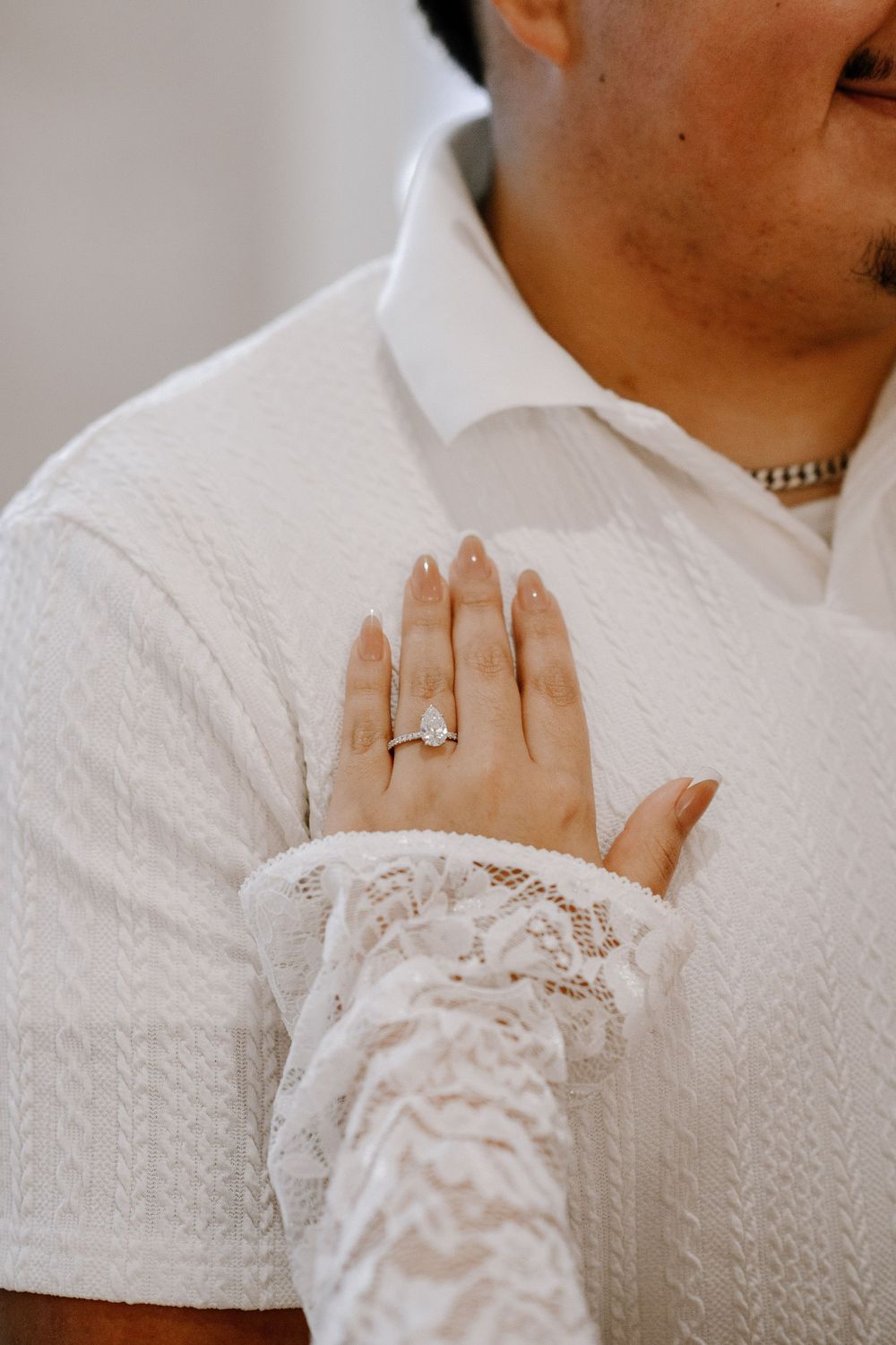 Close-up of a person wearing a white sweater showing off an engagement ring with delicate lace sleeve details.