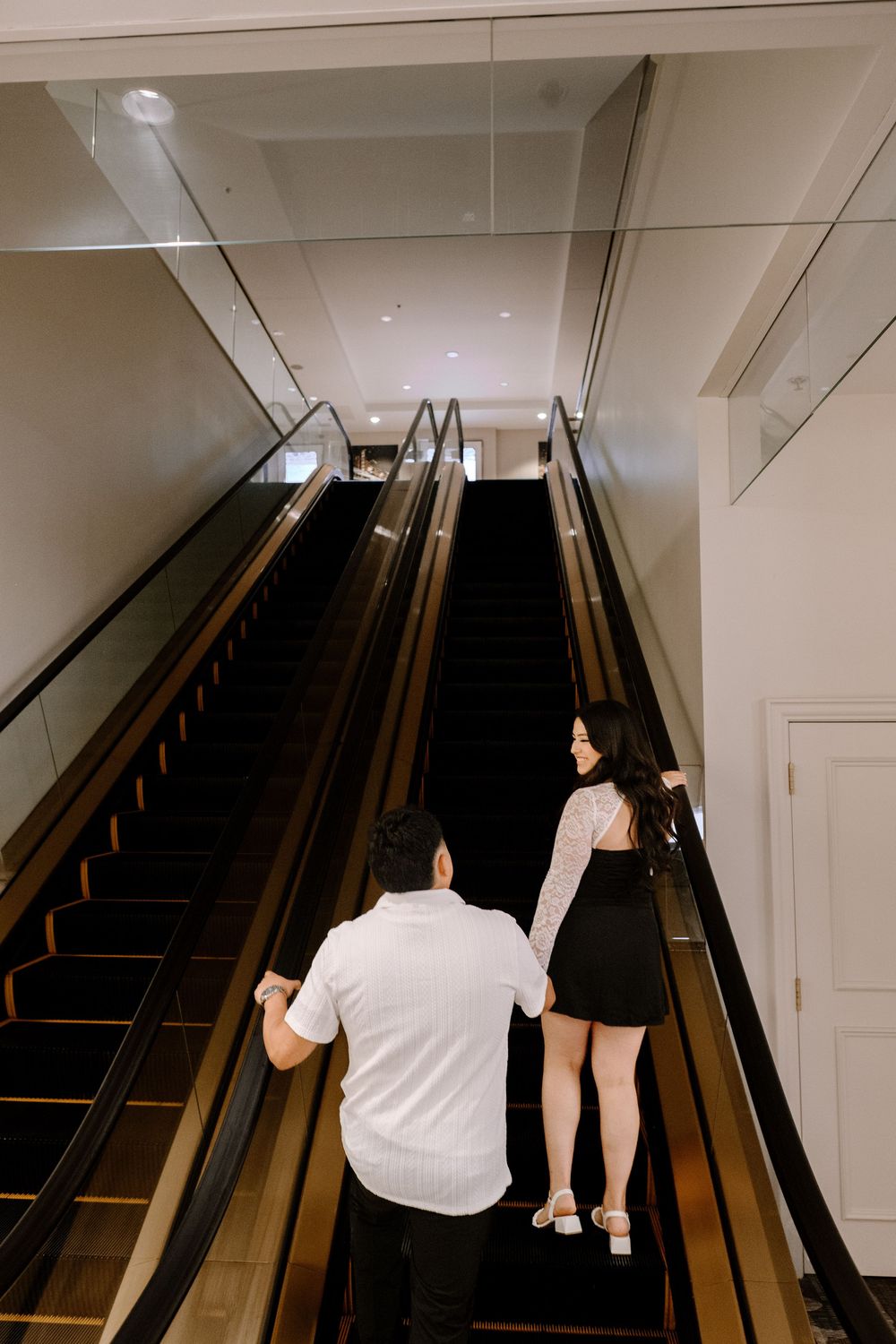 Two people ascending a dark wooden staircase with dramatic lighting and modern interior design elements.
