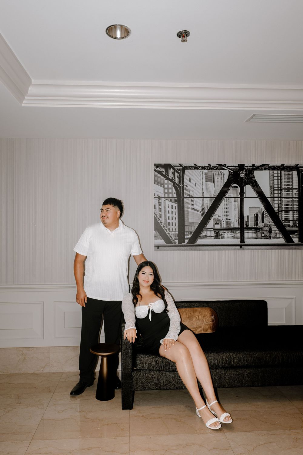 A minimalist interior scene with people in white and black attire sitting against a light-colored wall.