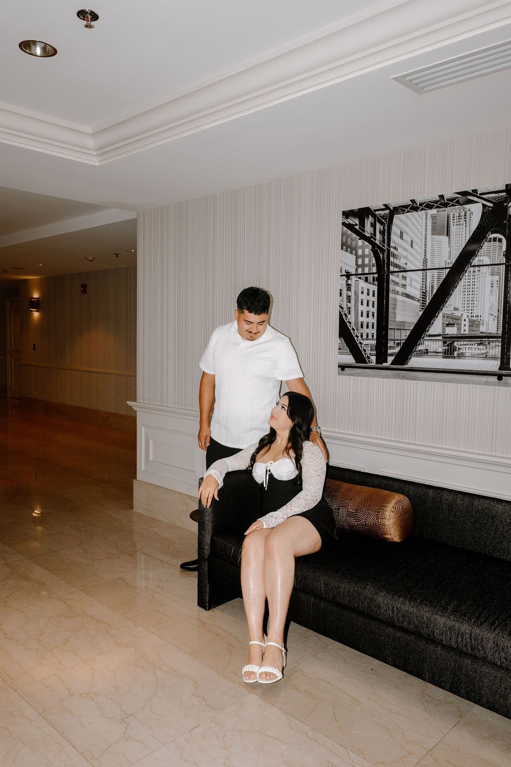 Two people in white shirts sitting together on a black couch in a minimalist room with monochrome artwork.