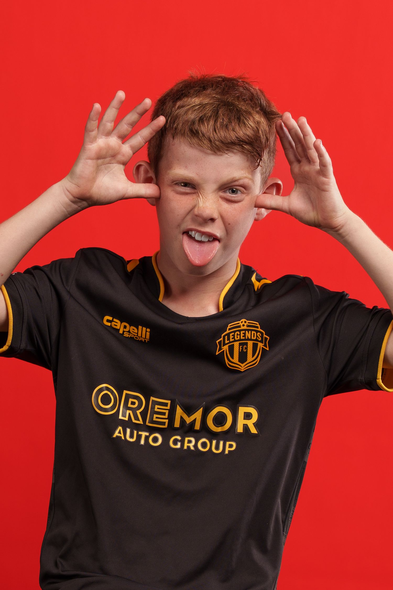 Young person in black and gold jersey making playful expressions against red background.