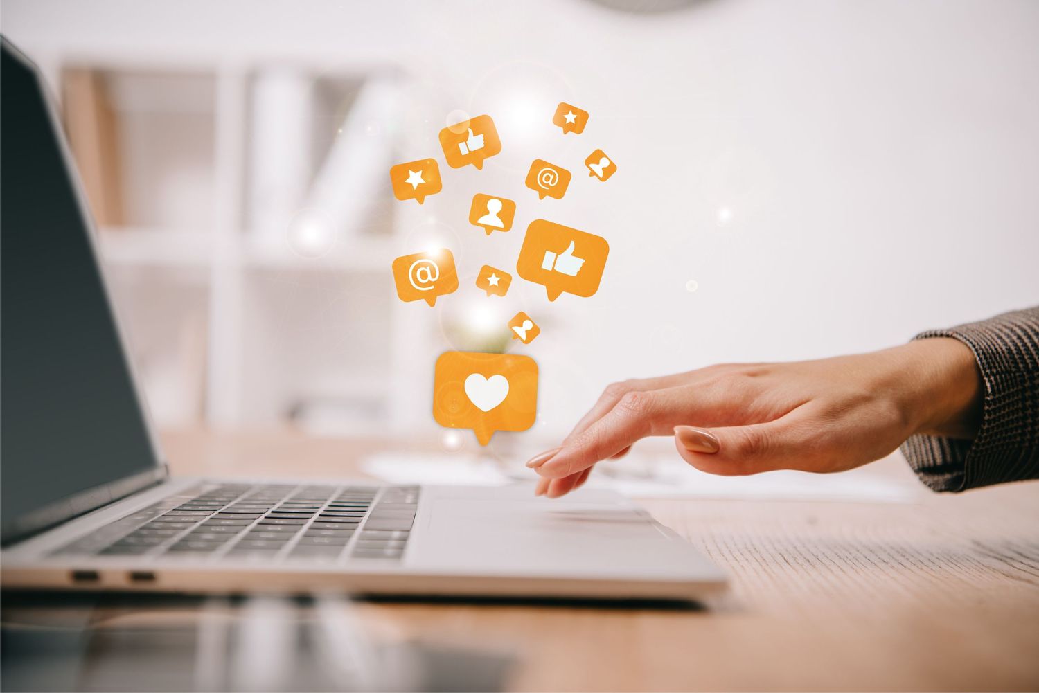 Hand typing on laptop keyboard while social media notification icons float above in orange glowing design.