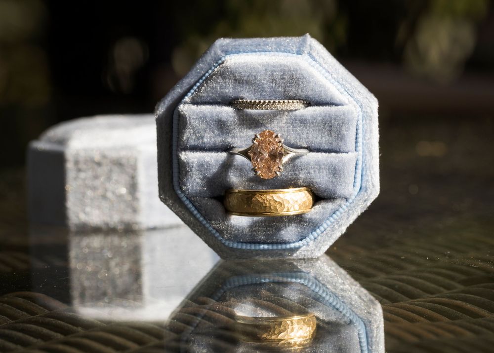 Wedding rings and engagement ring displayed in a gray velvet octagonal ring box with reflection on glass surface.