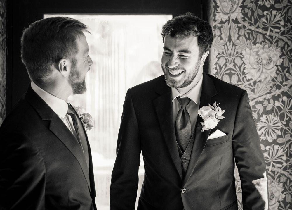 Four candid black and white photos showing groomsmen laughing and interacting during wedding preparations.