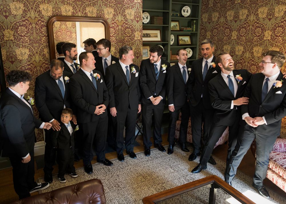 A group of formally dressed people line up against a patterned wallpaper background.