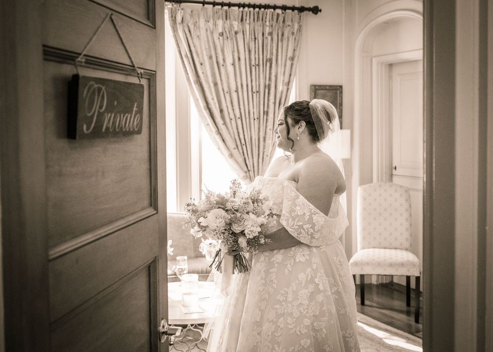 Elegant wedding dress hanging in doorway captured in romantic sepia tones.