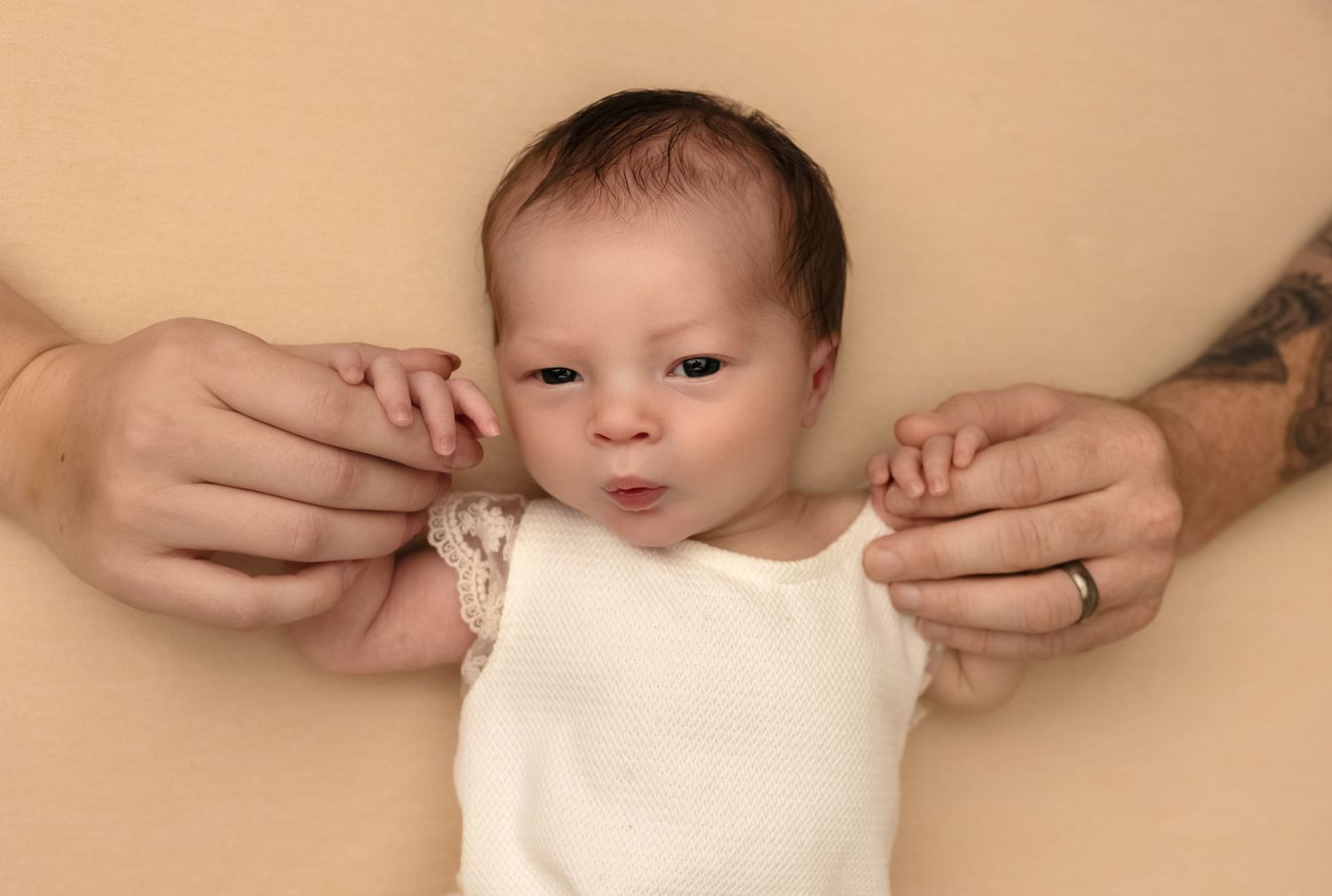 Parents hold their new baby's hands as she looks at the camera and lies on a warm blanket, captured by Charlottesville baby photographer.
