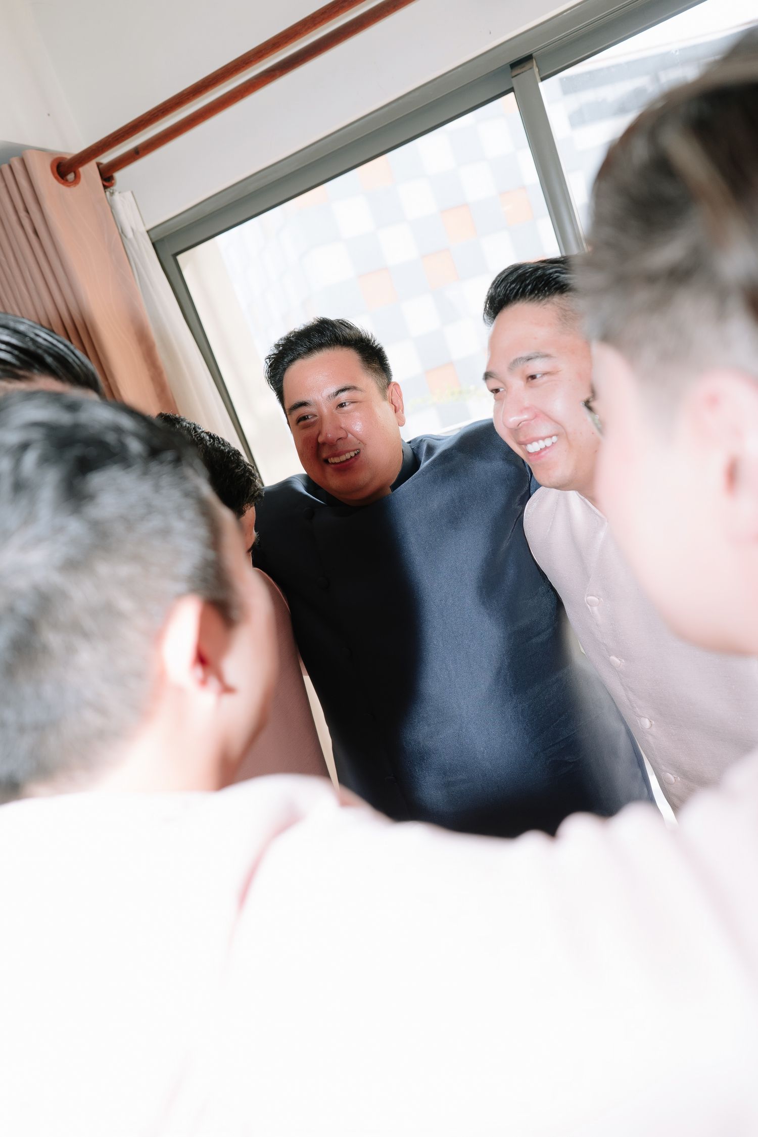 Smiling groom and groomsman sharing a cheerful moment together during wedding preparations indoors.