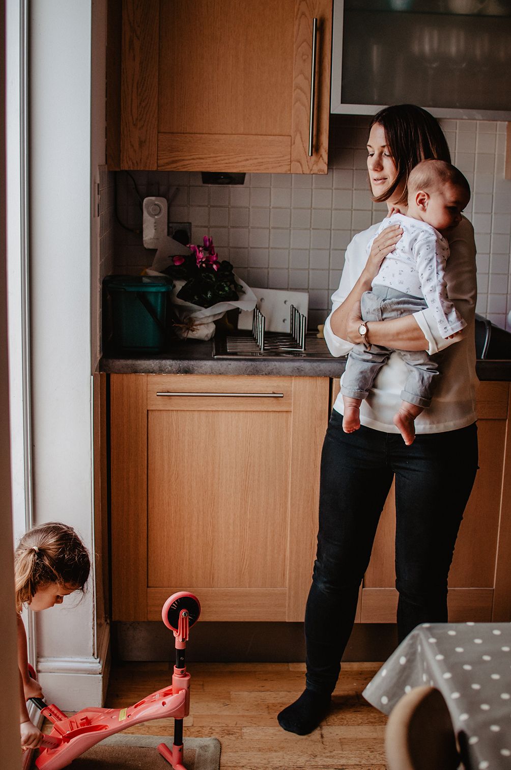 Interior view of a kitchen with wooden cabinets showing adults and children in a casual home setting.