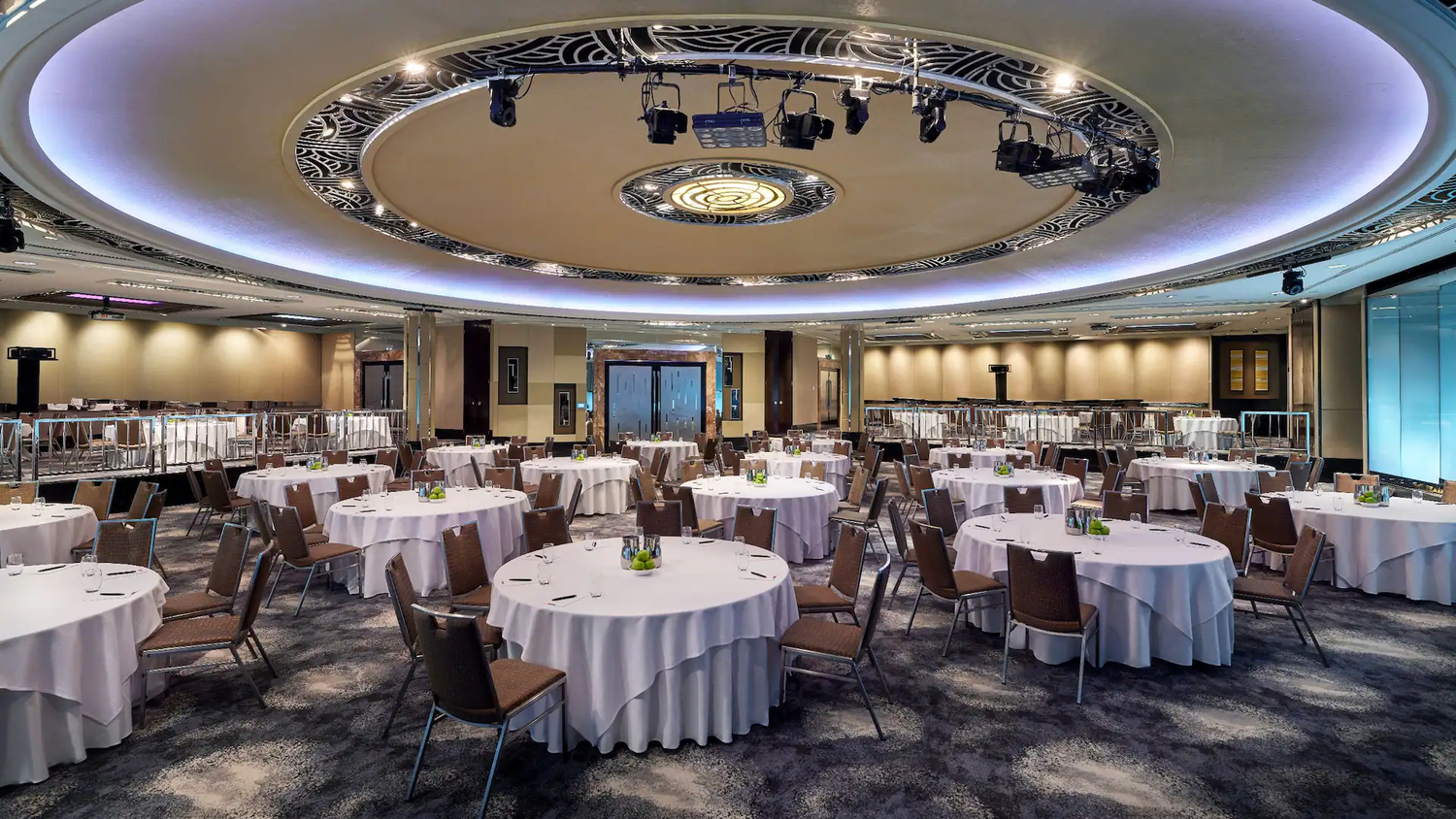 Modern banquet hall with circular lighting fixtures, round dining tables, and contemporary decor in elegant earth tones.