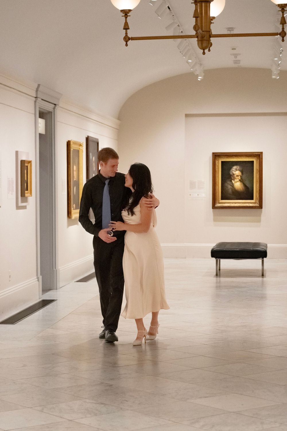 Couple dancing in an elegant art gallery with framed paintings on white walls.