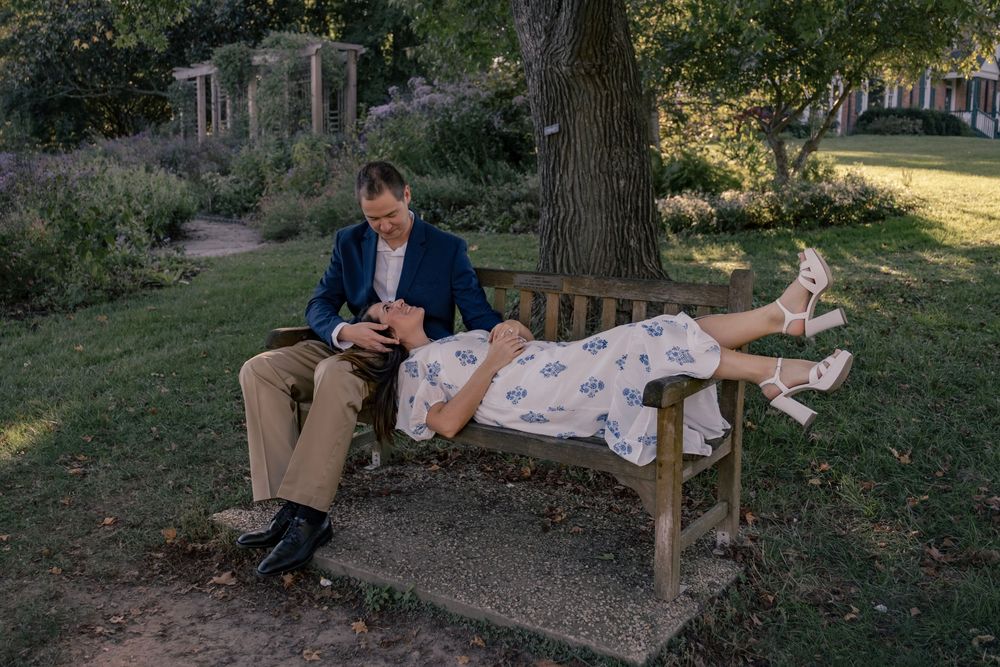 A couple relaxes together on a wooden bench in a serene garden setting during golden hour.