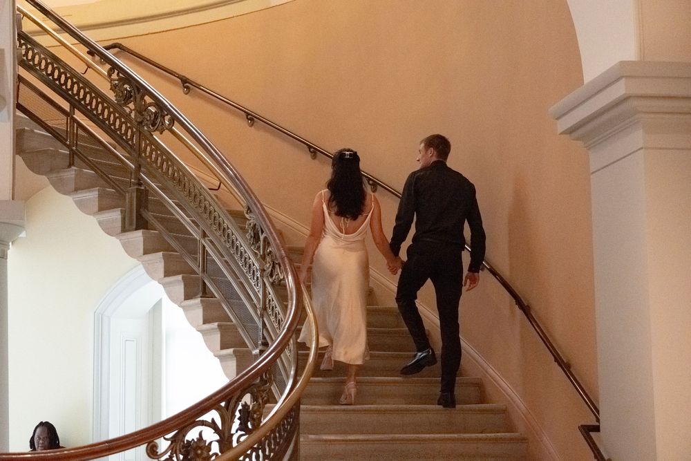 Romantic couple ascending a grand marble staircase in an elegant building.