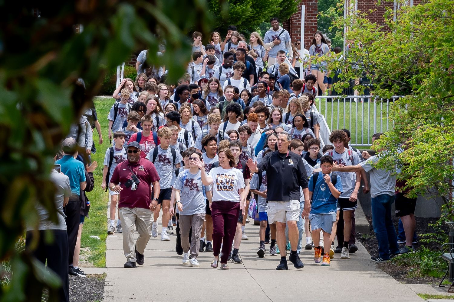 A large crowd of students walks across a university campus pathway during a sunny day.