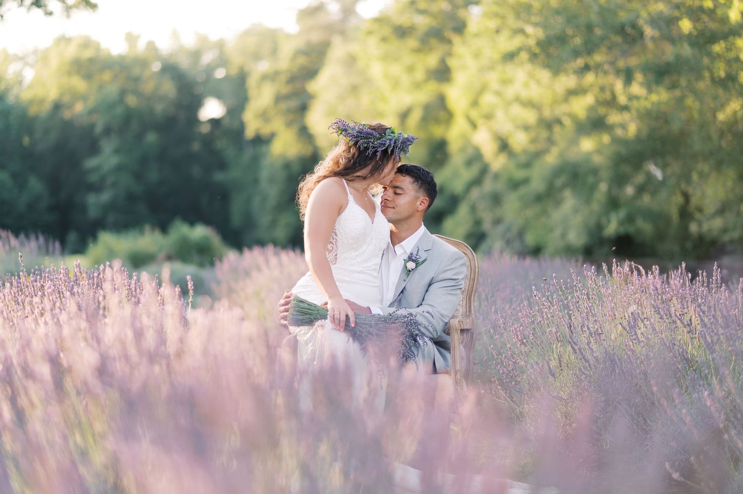 A wooden hexagonal wedding arch with white fabric draped stands in a lavender field on a sunny day.