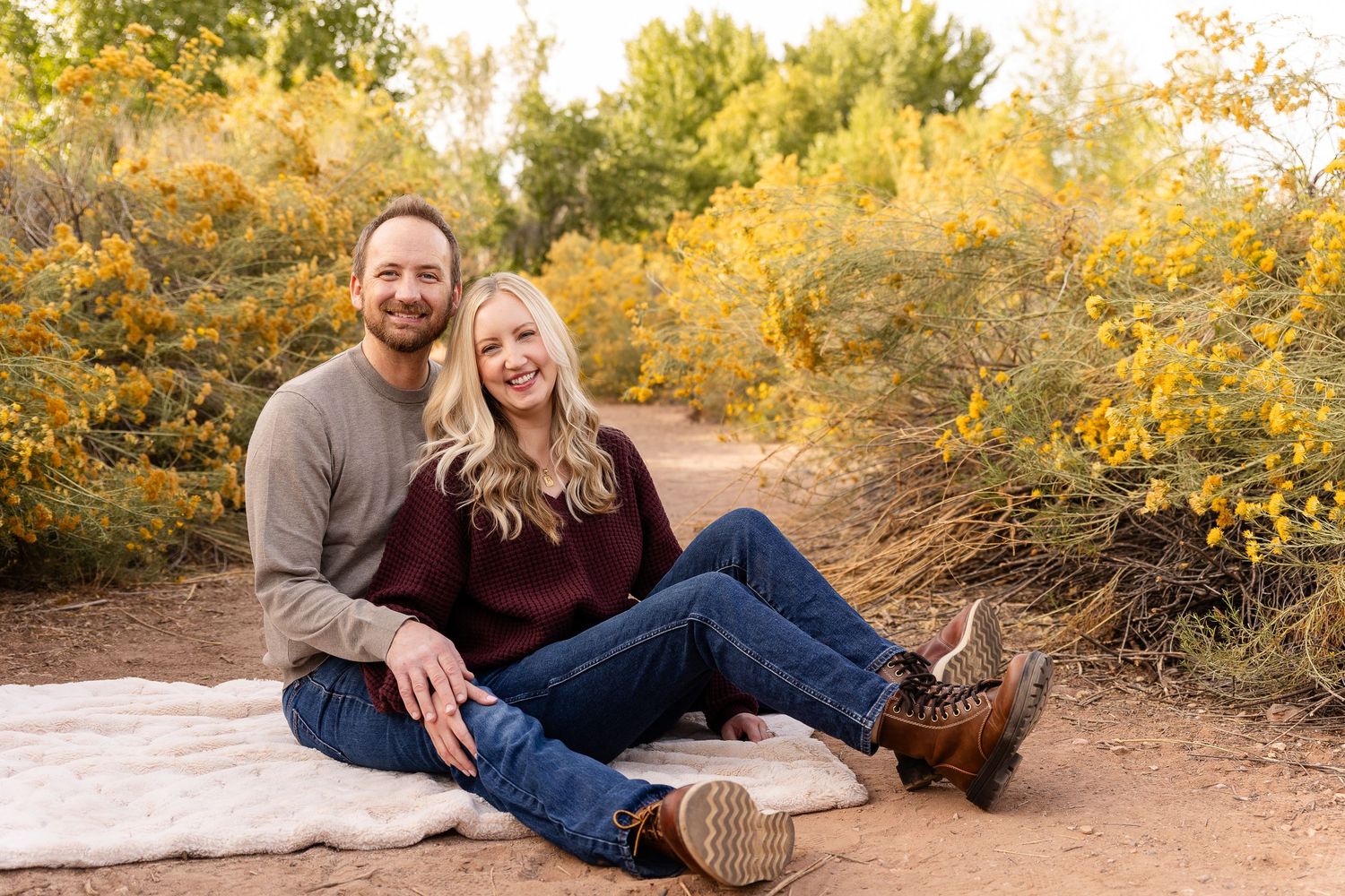 a couple sitting on blanket smiling at the camera with yellow desert blooms all around