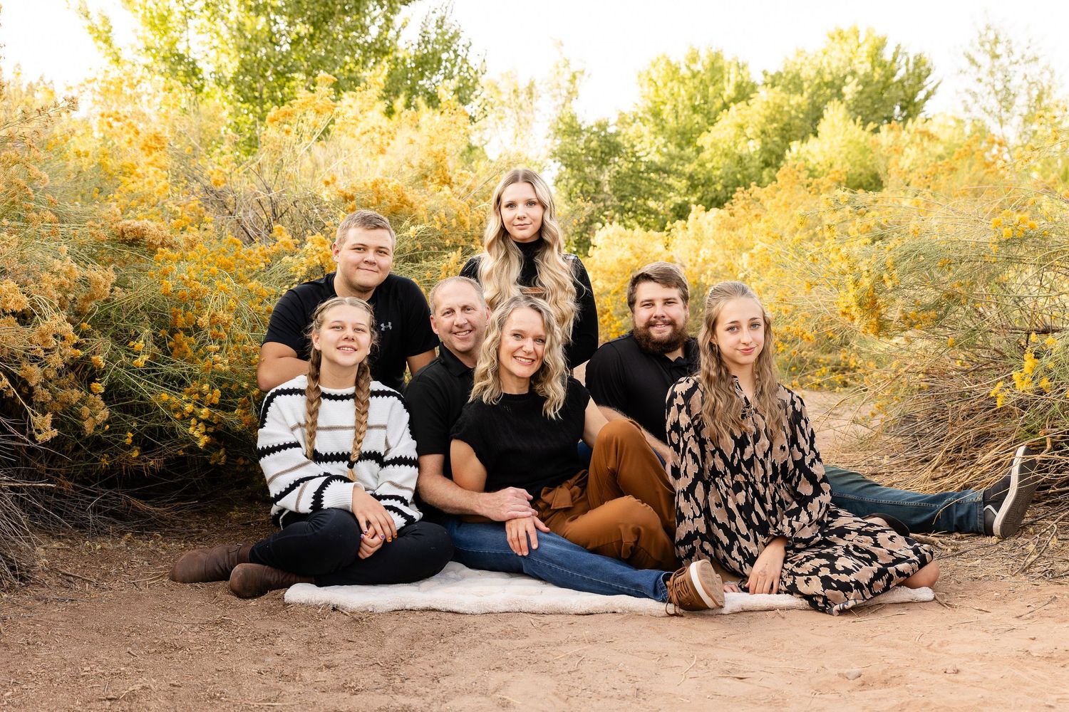 southern utah family photos with 5 grown children sitting on a blanket in fall colors surrounded by yellow desert blooms