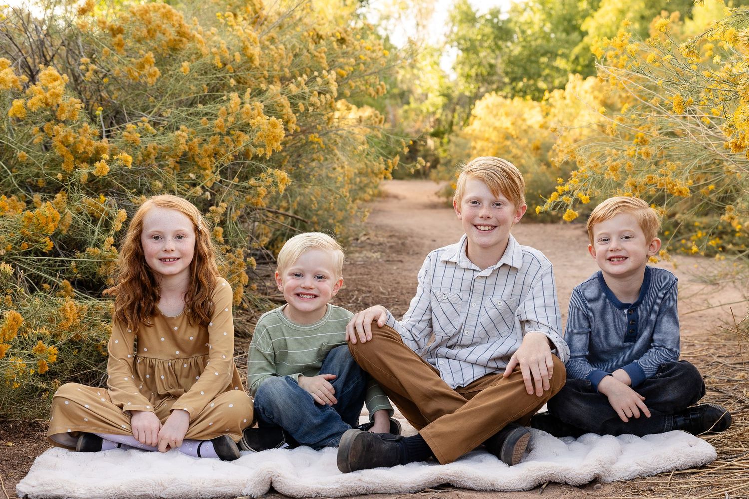 Tonaquint nature center siblings 4 kids smiling at the camera sitting on a blanket surrounded by yellow fall blooms St. George utah