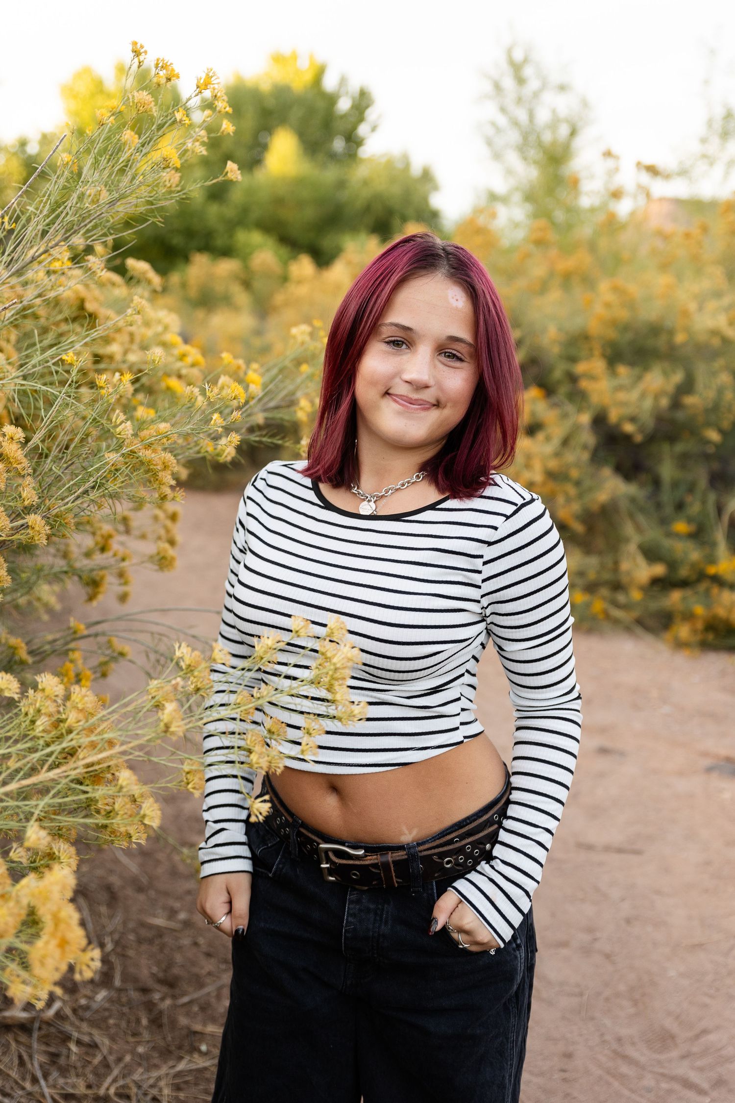 a teenage girl with red hair smiling at the camera next to yellow desert blooms