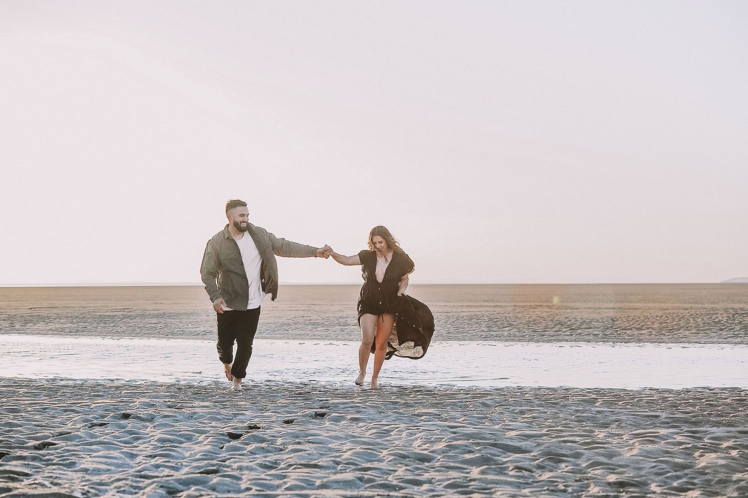 Couple enjoying playful moments together on vast sandy beach.