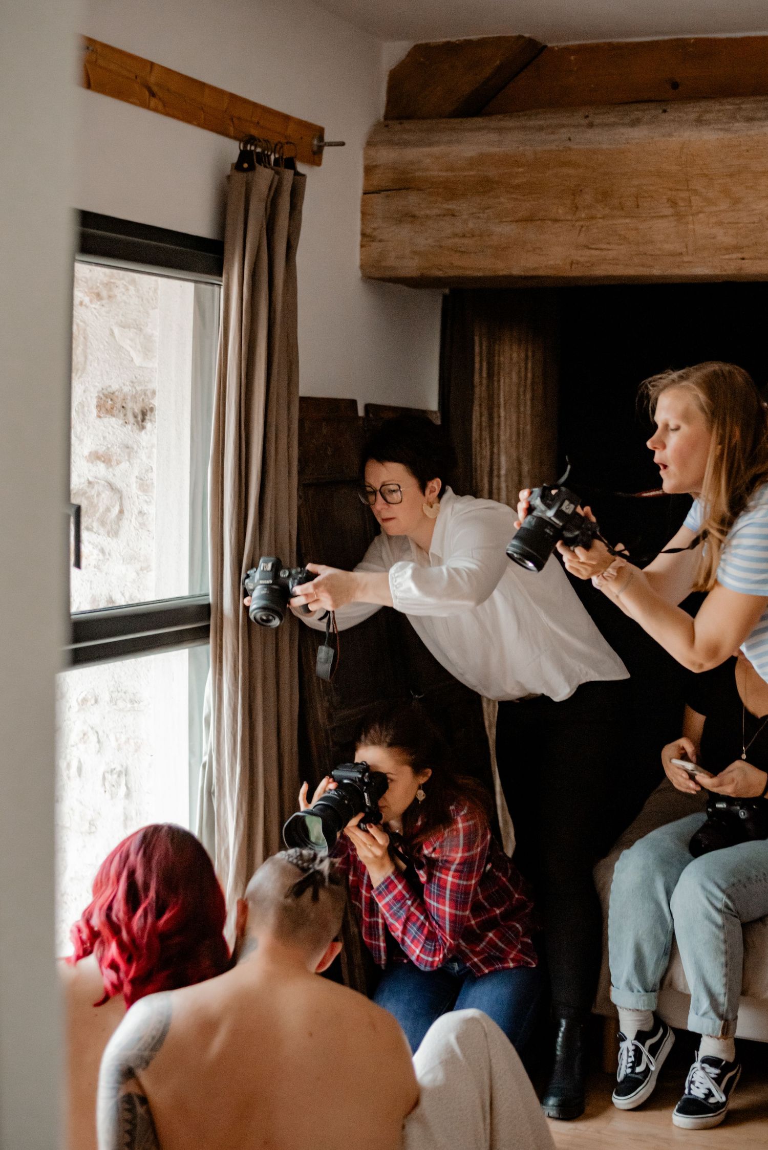 Group of photographers gather by a window during a photoshoot session with their cameras drawn.