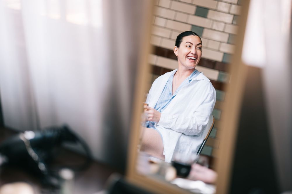 Person wearing a white robe smiles while getting ready in front of a mirror.
