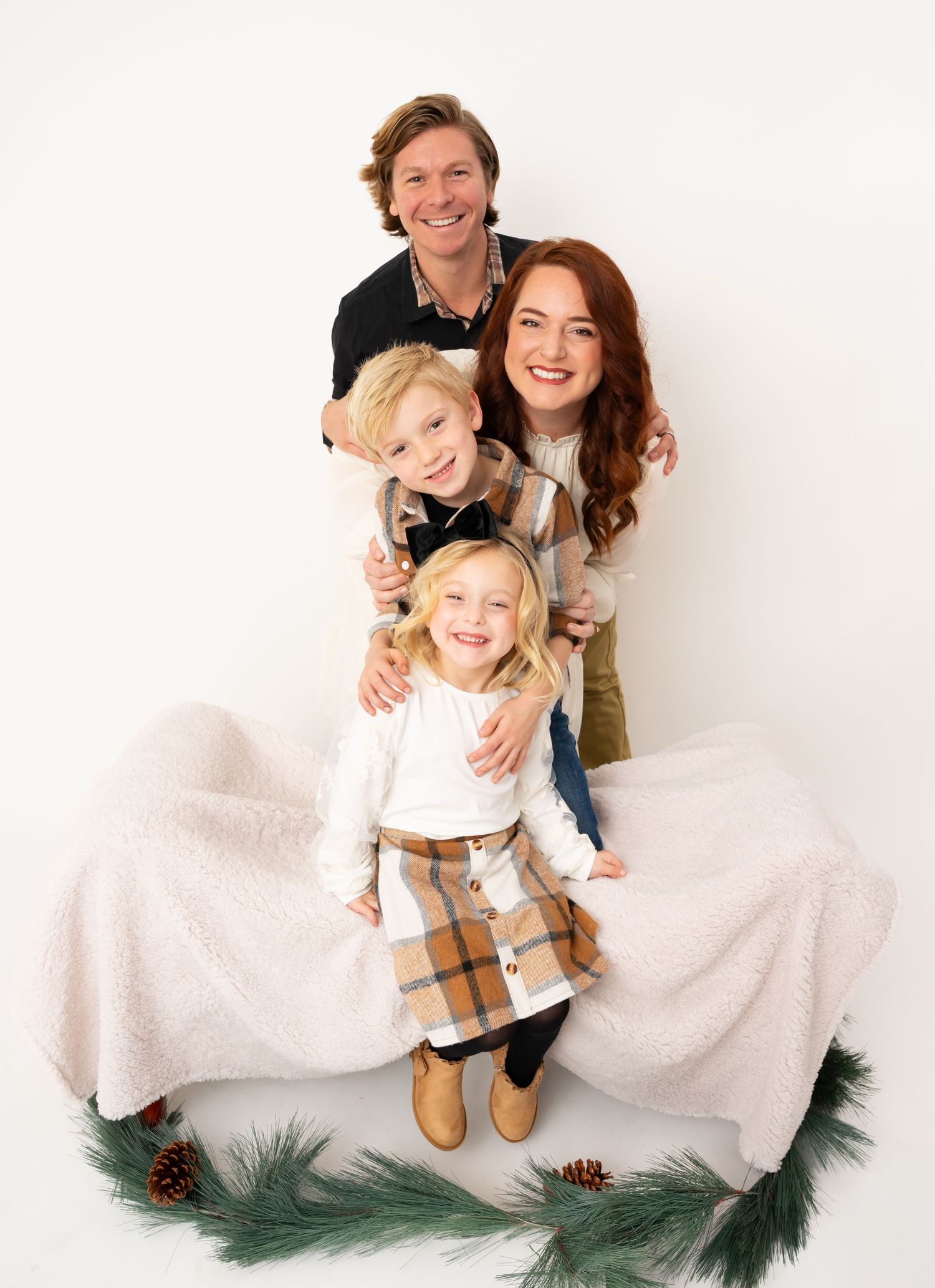 Family poses joyfully with white fabric and pine branches in holiday photo session.