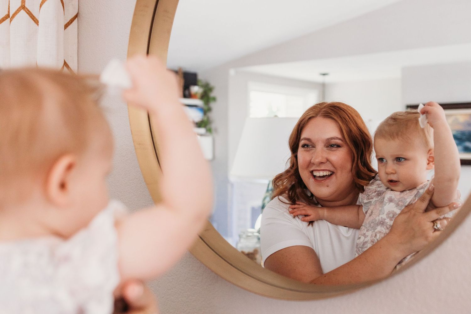 Baby's reflection shows in a round mirror mounted on a bathroom wall during daily hygiene routine.