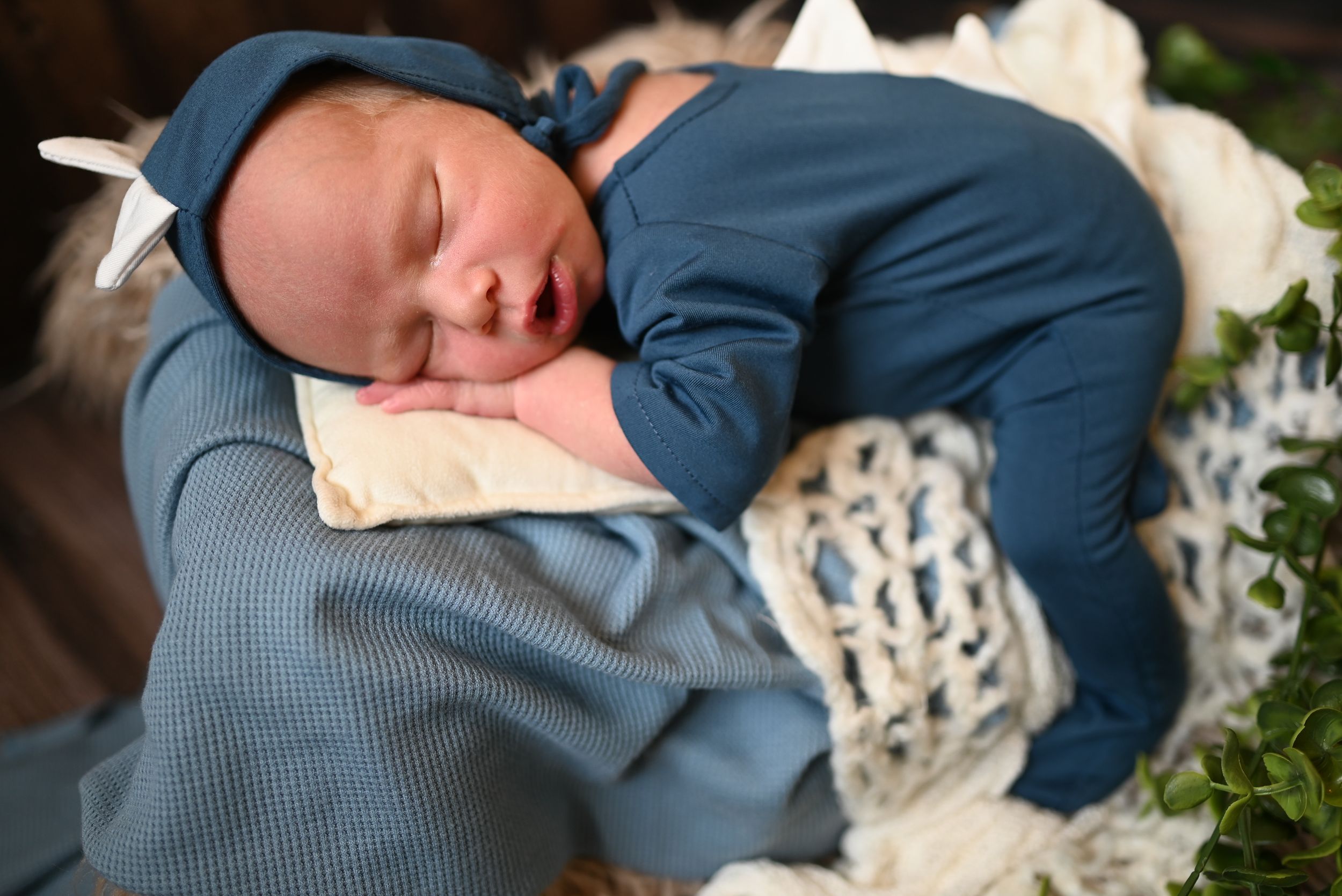 A sleeping infant wearing a cozy blue outfit rests on a textured white blanket.
