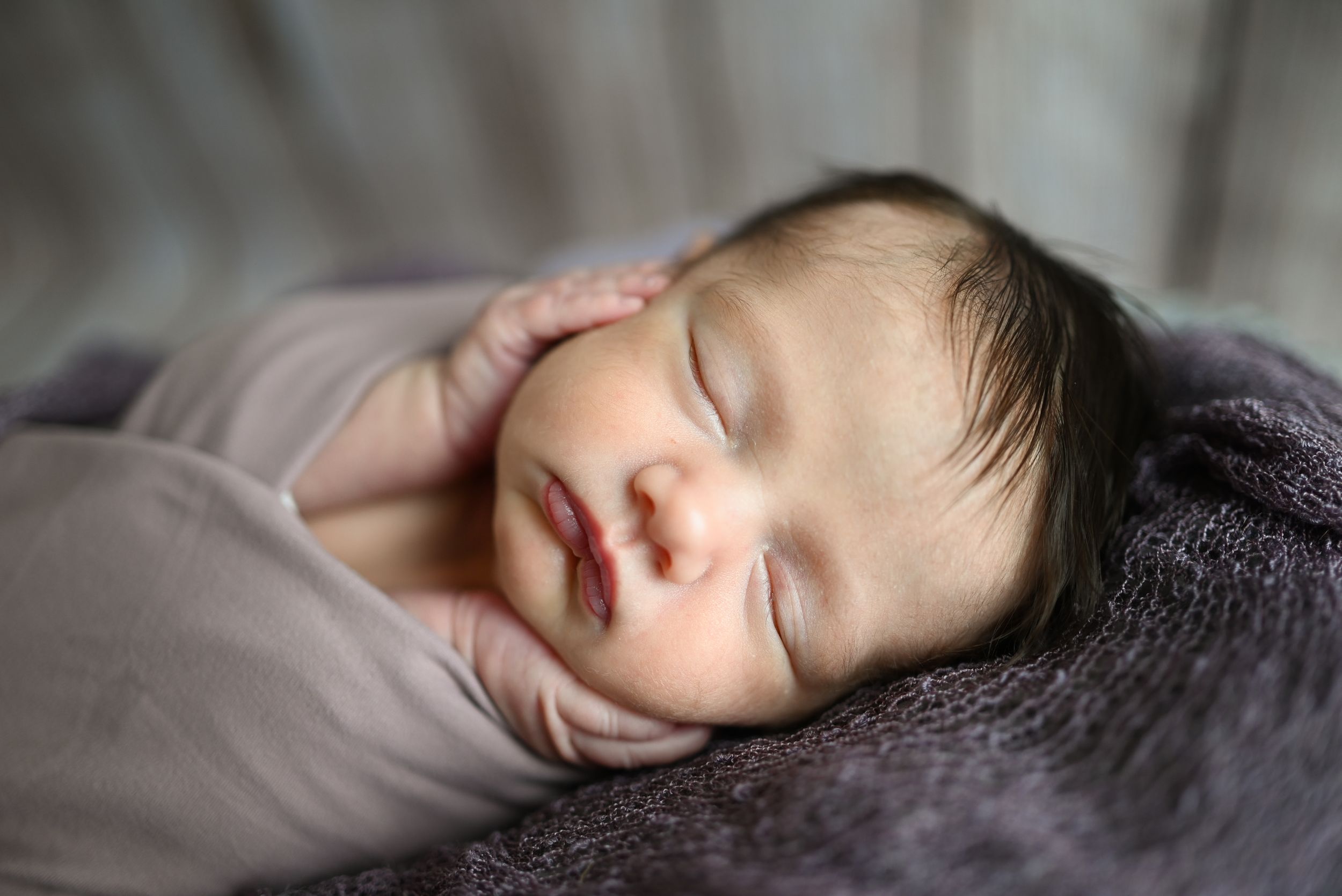 A peaceful newborn baby sleeping peacefully on soft gray blankets in natural window light.