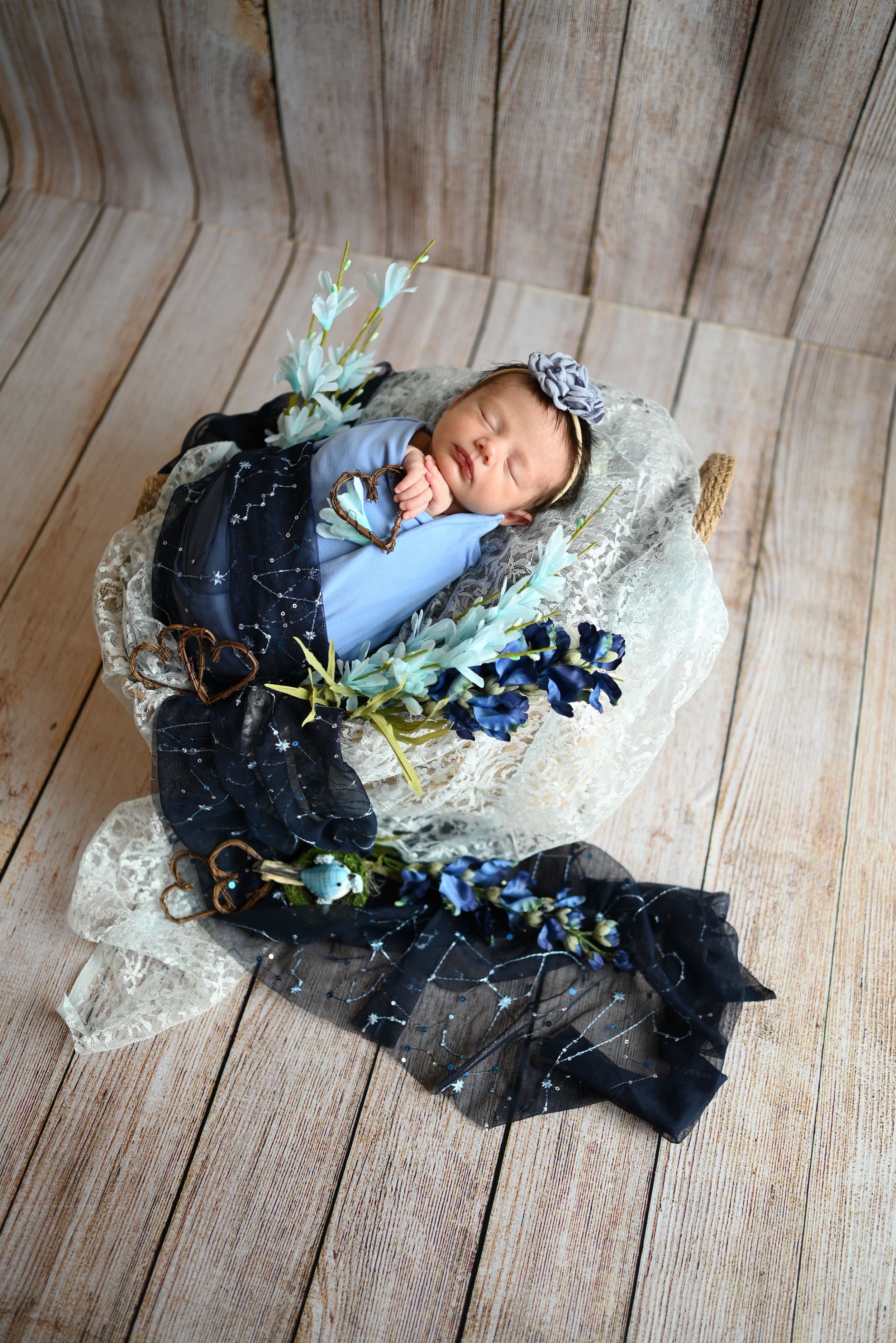 A series of baby photos with blue flowers and lace decorations on a wooden floor background.