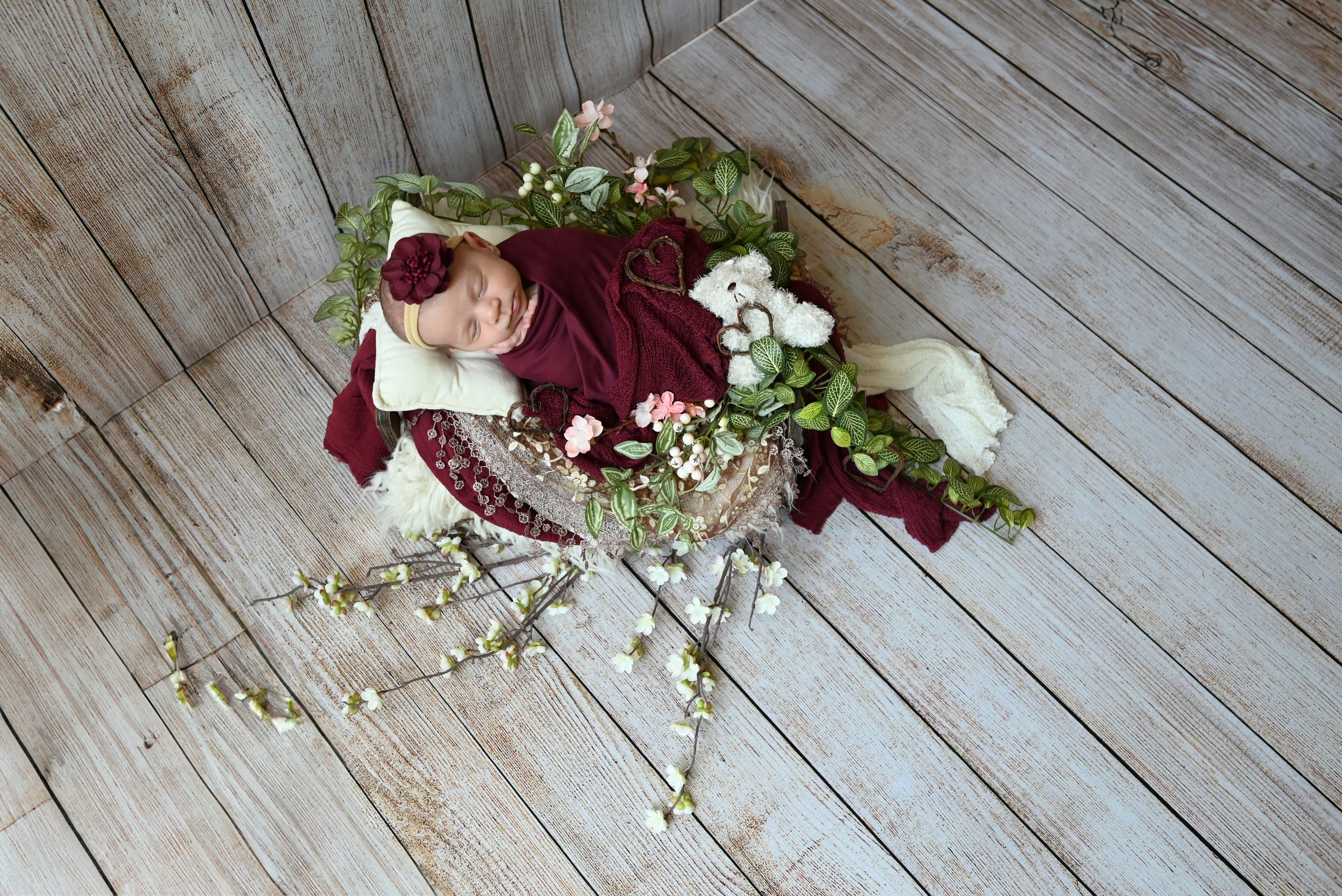 White floral decorations and burgundy rose petals scattered on a rustic wooden plank backdrop.